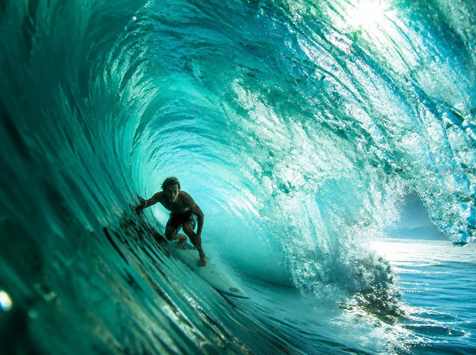 Surfer riding inside a large turquoise ocean wave